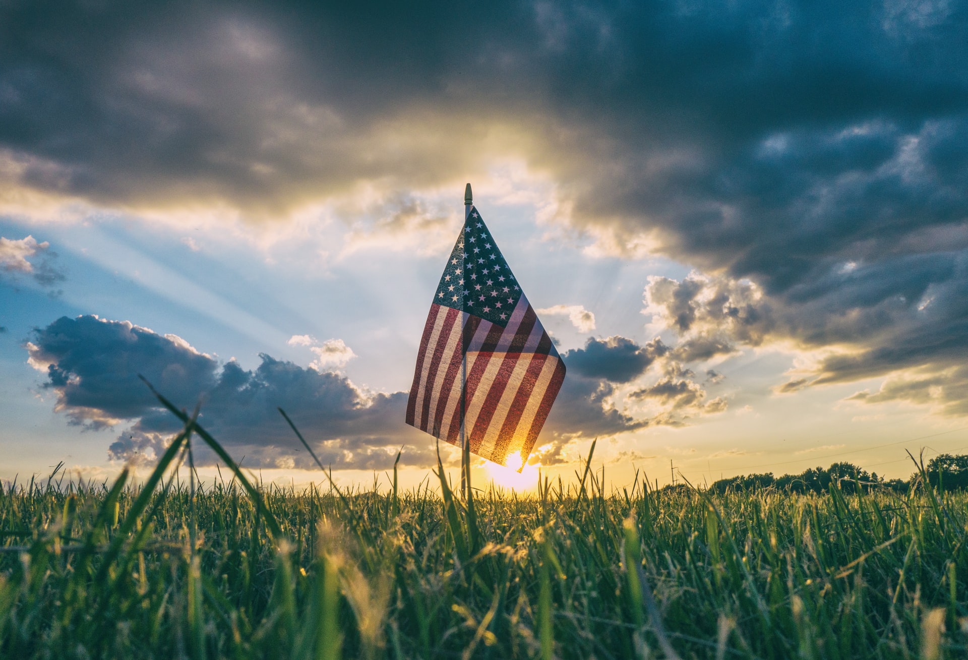 Small American flag placed in the ground with a sunset in the background