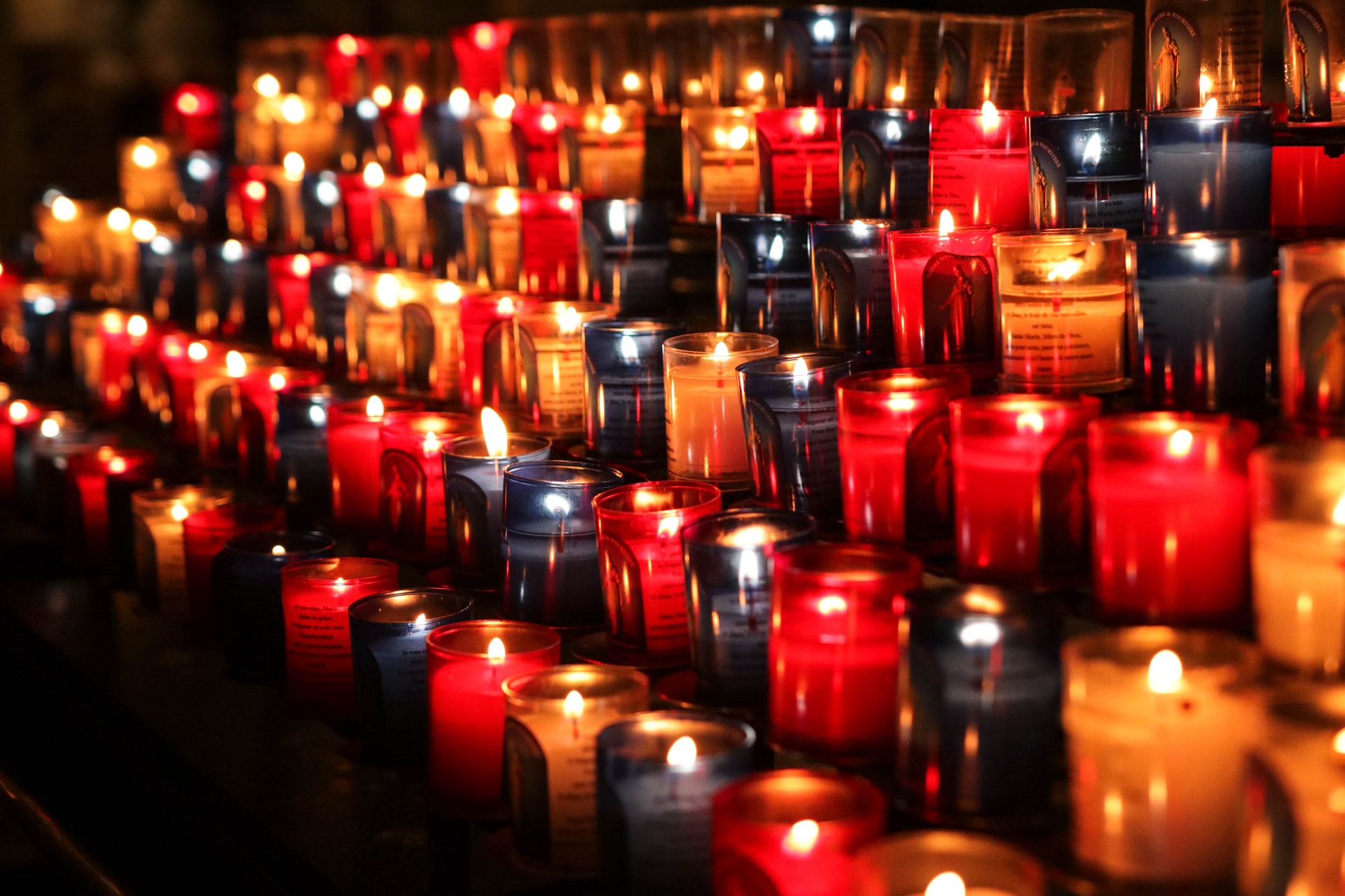 Rows of lit candles in red, yellow, and black circular glass containers