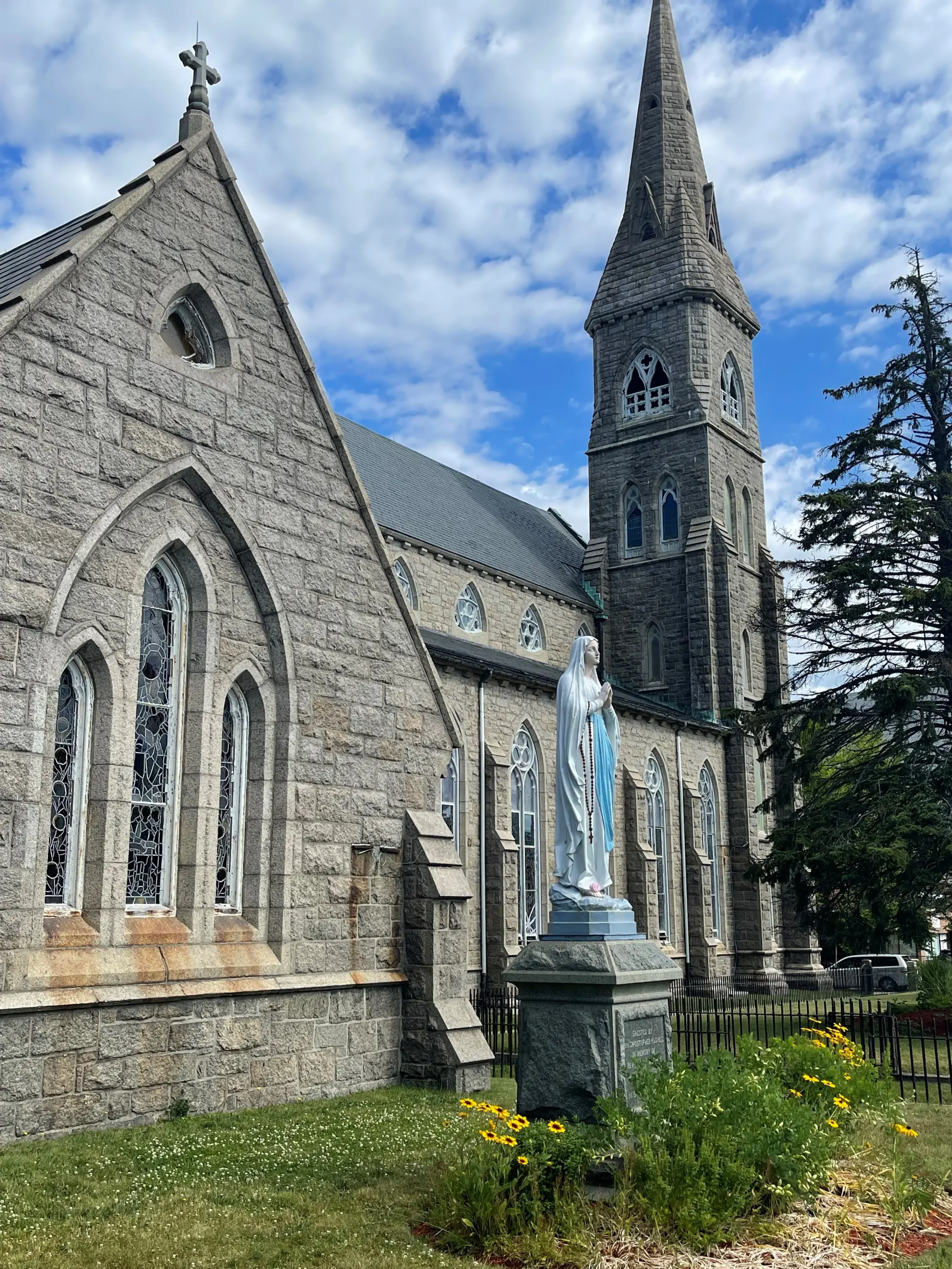 Side view of the Cathedral, a statue of Mary praying surrounded by yellow flowers