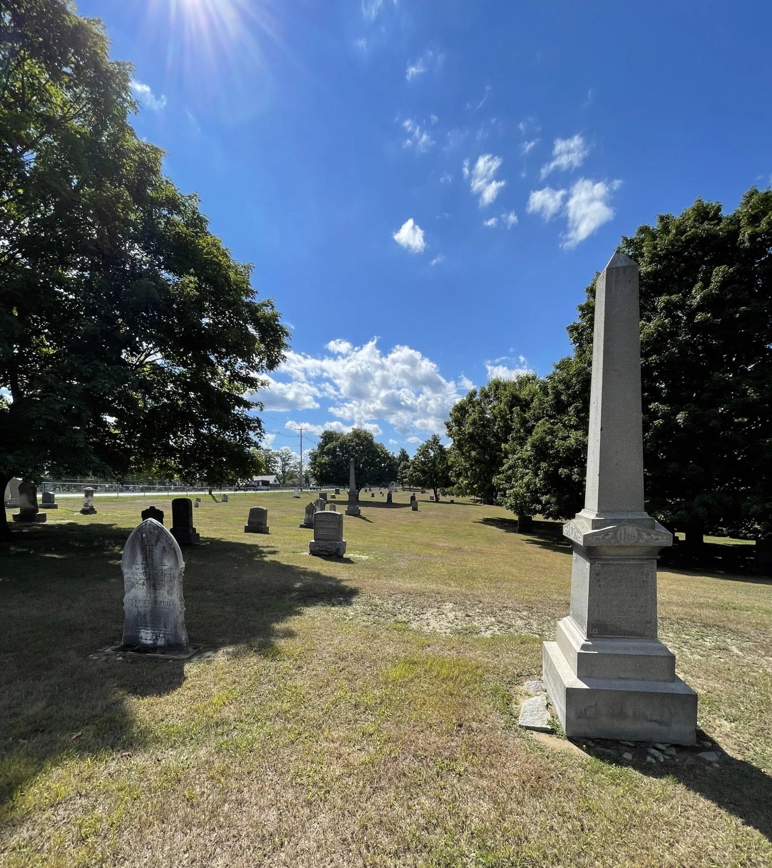 Obelisk and other headstones under a blue sky and sunshine.
